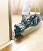 A person wearing gloves is using a cordless oscillating tool to cut a piece of wood trim near a doorway. Produktbild-Vorschau