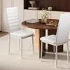 Two white dining chairs are placed around a round wooden dining table in a well-lit room. Náhled obrázku produktu