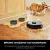 A robot vacuum cleaner is cleaning up pet hair on a wooden floor next to a dog's food bowls. A corgi dog is in the background. Produktbild-Vorschau
