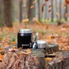 A black Meteor thermobehälter with a silver lid and spoon sits on a tree stump in a forest setting with fallen autumn leaves. Náhled obrázku produktu
