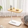 C-förmiger Beistelltisch aus hellem Holz und Weiß mit Glasvase, kleinem Getränk und Sandwich darauf, neben einem beigen Kissen und einer Hahnentritt-Decke Voir les images du produit