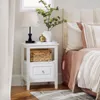 A white nightstand next to a bed with pink and white bedding. Náhľad obrázku produktu