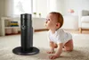A baby crawling on a carpet looking at a black humidifier with mist coming out. Produktbild-Vorschau