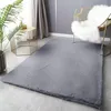 A plush gray rug is laid out on a light gray floor in a modern living room setting. A gold wire chair with a white fluffy throw is placed on the rug, and a small gold hexagonal side table with a plant and a decorative deer figurine is next to the rug. Produktbild-Vorschau