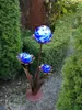 A garden decoration with glass spheres on metal stems, surrounded by greenery. Anteprima dell’immagine prodotto