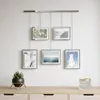 A wall display of five framed pictures above a wooden dresser with a plant and a candle holder. Podgląd zdjęcia produktu