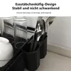 A close-up view of a black dish drying rack with glasses, a bowl, and cutlery in its holders. Produktbild-Vorschau