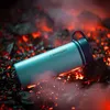 A turquoise thermos bottle is placed on glowing red coals and black rocks, with smoke or steam rising. Podgląd zdjęcia produktu