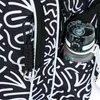 A close-up view of a backpack with a black and white abstract pattern. A water bottle is visible in a side pocket, and a carabiner with a paracord keychain is attached to the front. Podgląd zdjęcia produktu