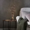 A decorative set of LED twig lights in a vase on a side table next to a sofa. Podgląd zdjęcia produktu