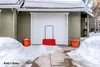 A snow shovel leaning against a garage door during winter. Produktbild-Vorschau