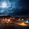 A nighttime beach scene with illuminated spherical lights and dining tables set up for a romantic dinner. Náhľad obrázku produktu