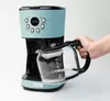 A hand is holding a glass coffee pot next to a turquoise coffee maker. Anteprima dell’immagine prodotto