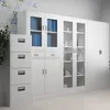 A row of white metal storage cabinets, including a four-drawer filing cabinet and glass-fronted cabinets, displayed in an office setting. Anteprima dell’immagine prodotto