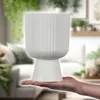 A hand holds a white planter in a living room setting. Podgląd zdjęcia produktu