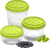 Three clear plastic food storage containers with green lids are arranged on a white background, with a small pile of sunflower seeds and a sprig of basil in the foreground. Náhľad obrázku produktu