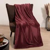 A plush burgundy blanket draped over a brown armchair, with a cup of tea and dried flowers in the background. Produktbild-Vorschau
