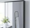 A mirror with a matte black frame reflects a towel rack and a plant on a windowsill. Produktbild-Vorschau