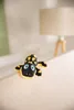 A plush toy salamander is lying on a white surface, with a blurred lamp in the background. Produktbild-Vorschau