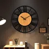 A wall clock with Roman numerals is mounted on a dark gray wall above a shelf with decorative items. Produktbild-Vorschau