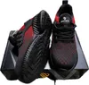 A pair of black and red safety shoes are displayed on a black box. Produktbild-Vorschau