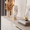 A close-up of a white dresser with decorative items on top, including a bust, dried flowers, and books. Produktbild-Vorschau