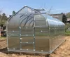 A greenhouse is set up outdoors on a patch of dirt with some trees and buildings in the background. Produktbild-Vorschau