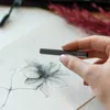 A hand holding a charcoal stick over a drawing of a flower. Podgląd zdjęcia produktu