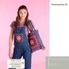 A woman wearing denim overalls and holding a crocheted tote bag, with a pink background. Produktbild-Vorschau