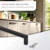 Close-up of black cabinet handles and screws, with a kitchen scene in the background. Produktbild-Vorschau