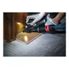 A person wearing white gloves is using an oscillating multi-tool with a vacuum attachment to cut a piece of wood near a wooden cabinet and floor. Voir les images du produit