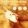 A child's hands holding a glowing bunny-shaped night light on a fuzzy brown blanket. Produktbild-Vorschau