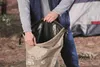 A person is holding open a tan bag with a black interior, possibly packing or unpacking camping gear. Podgląd zdjęcia produktu