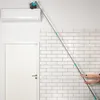 A person is using a telescopic duster to clean the top of an air conditioning unit mounted on a white wall with subway tiles. Podgląd zdjęcia produktu