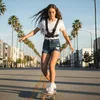 A woman is skateboarding down a street lined with palm trees. Náhľad obrázku produktu