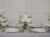 A formal table setting with white plates, silverware, and white floral arrangements. Produktbild-Vorschau