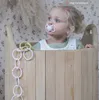 A baby sitting in a wooden basket with a pacifier and a toy chain. Produktbild-Vorschau