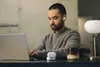 A man wearing earbuds is working on a laptop in a modern office or home office setting. Anteprima dell’immagine prodotto