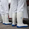A row of people wearing white protective suits and white boots with blue soles. Produktbild-Vorschau