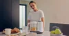 A woman is preparing baby food in a kitchen using a multifunctional food processor. Produktbild-Vorschau