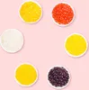 Six small white bowls filled with colorful popping boba pearls arranged in a circular pattern on a pink background. Produktbild-Vorschau