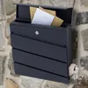 A dark gray mailbox mounted on a stone wall, filled with letters and a rolled-up newspaper. Produktbild-Vorschau