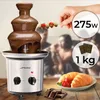 A chocolate fountain with fruit on a skewer, and croissants and strawberries on a plate, with people blurred in the background. Podgląd zdjęcia produktu