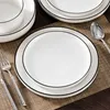 A set of white ceramic plates with a black rim, arranged on a brown placemat. Náhled obrázku produktu