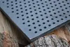 A close-up shot of a perforated metal grate resting on logs. Produktbild-Vorschau