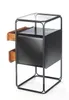 A modern side table with a black metal frame, a black cabinet, two wooden drawers, and a glass top, shown against a white background. Produktbild-Vorschau