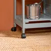 Close-up of the bottom of a gray kitchen cart with black wheels, resting on a woven rug. Produktbild-Vorschau
