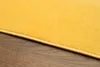 A close-up view of a yellow rug on a wooden floor. Voir les images du produit