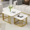 A set of two nesting square coffee tables with a white marble-look top and gold metal legs, placed in a living room setting next to a sofa. Náhľad obrázku produktu