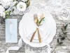 A beautifully set table with white plates, gold cutlery, and a white ribbon, suggesting a wedding or special occasion. Podgląd zdjęcia produktu